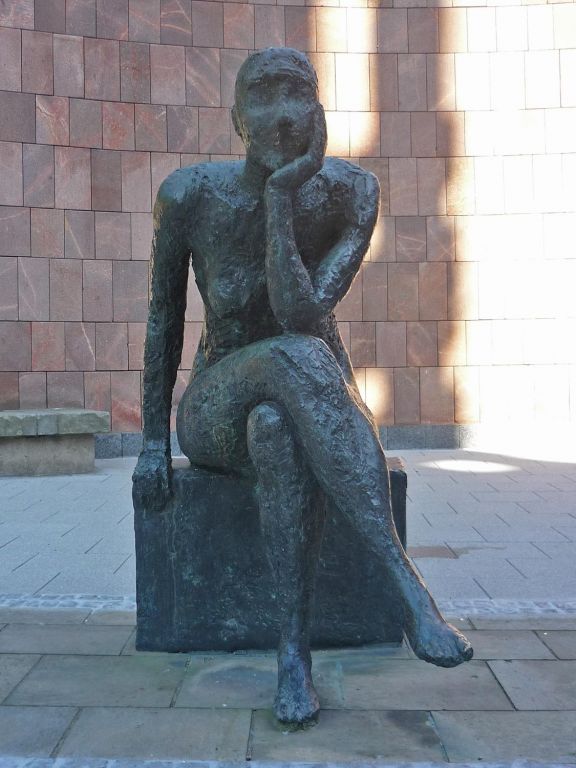 Vor der schützenden Wand aus rotem Porphyr sitzt die Sinnende auf einem eckigem Sockel