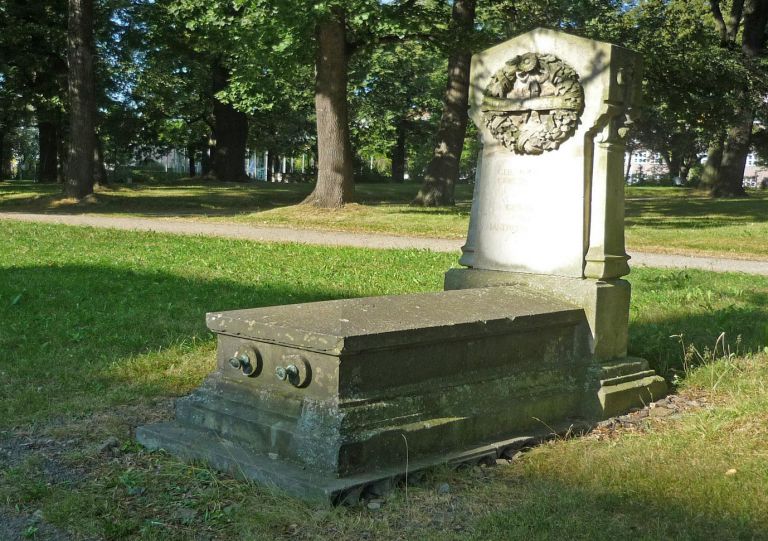 Blick auf ein Sandstein-Ehrengrab mit Gedenkstein
