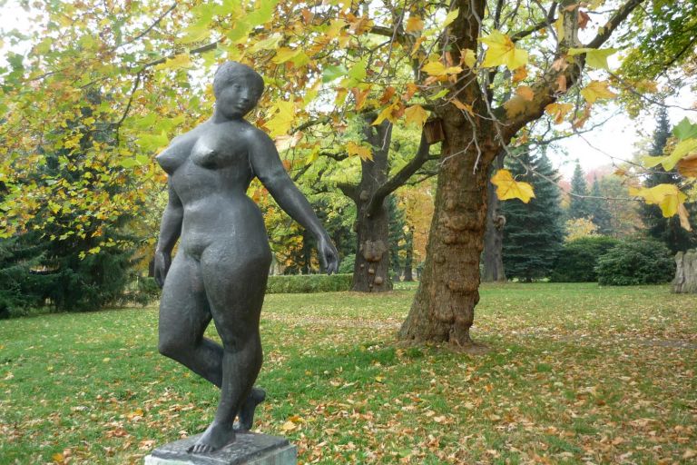 unter einer Platane auf einem Steinsockel steht die Bronzeplastik auf einer kleinen Plinte