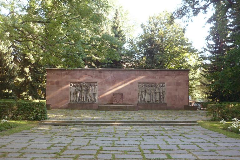 am Ende eines mit Natursteinplatten ausgelegten Platzes steht das Mahnmal aus rotem Rochlitzer Porphyr und zwei Personengruppen aus Sandstein